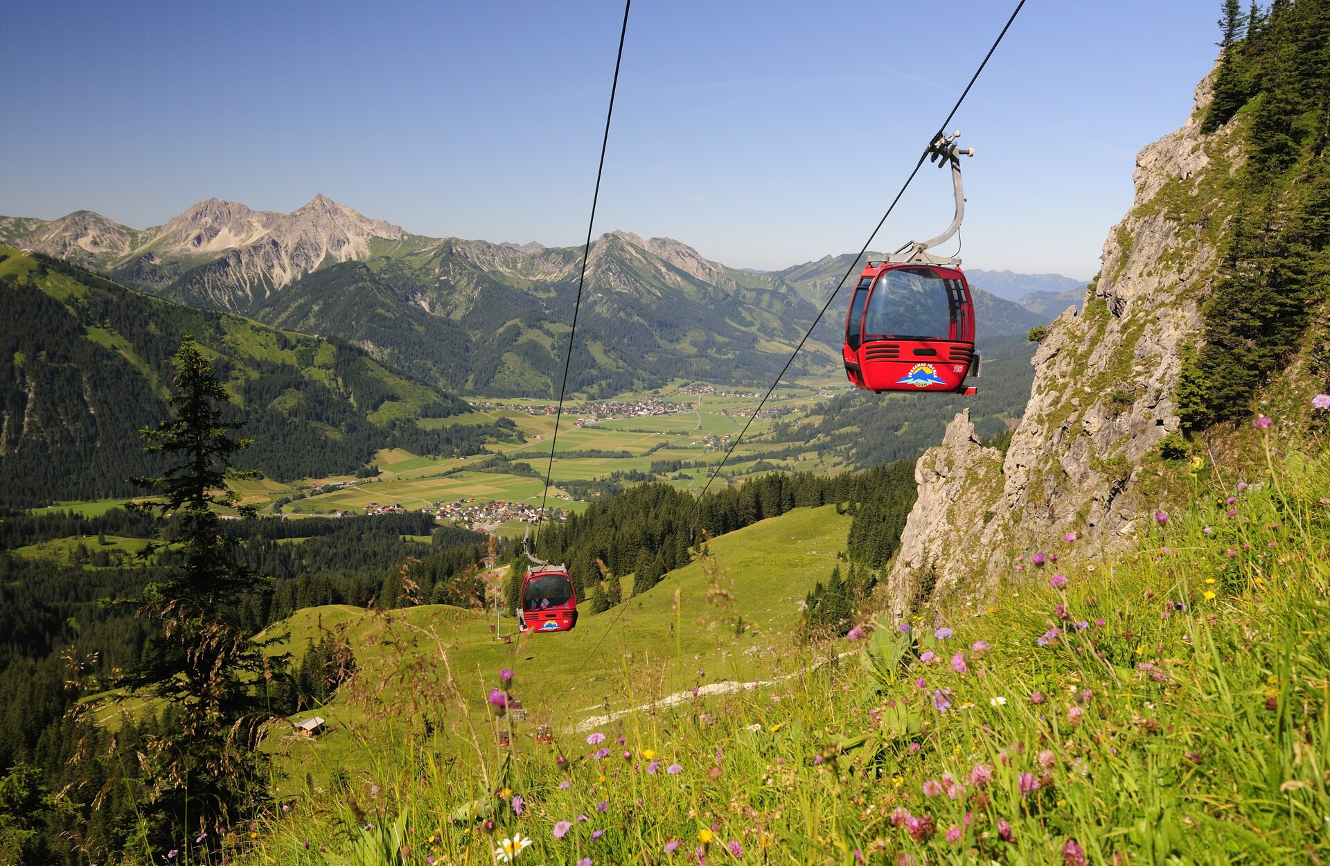 Rote Seilbahn vor Berglandschaft mit grünen Wiesen und blauem Himmel
