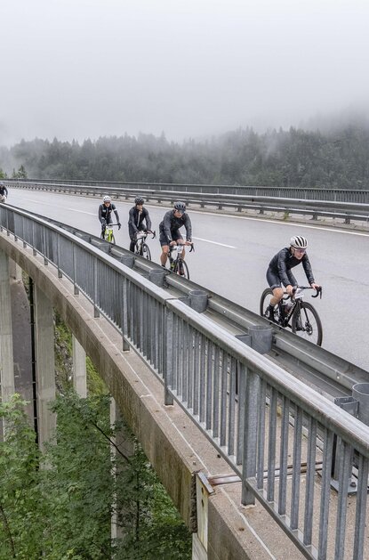 Radfahrer auf einer Brücke vor nebliger Berglandschaft