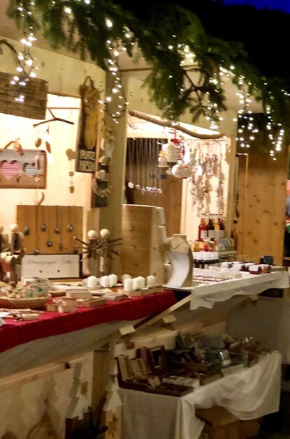 Adventsmarktstände mit weihnachtlicher Dekoration und Waren wie Schmuck und Kerzen bei Dämmerung