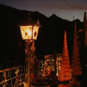 Beleuchtete Laterne und Deko-Weihnachtsbäume auf dem Adventmarkt Sonnenhof vor dunkler Bergkulisse