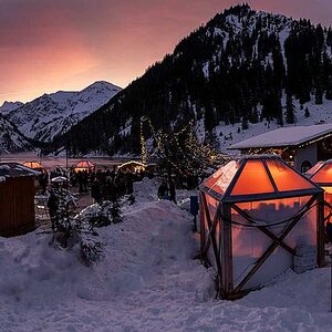 Vilsalpsee im Winter mit Weihnachtsmarktständen vor Bergkulisse im Abendrot