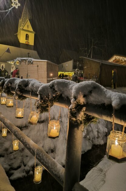 Verschneiter Weihnachtsmarkt in Jungholz mit Lichtern und Kirche im Hintergrund