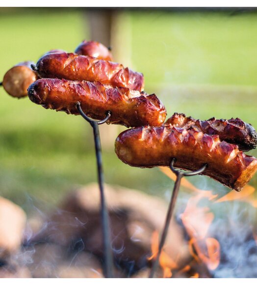 Würstchen und Zwiebeln am Spieß über offenem Feuer gegrillt