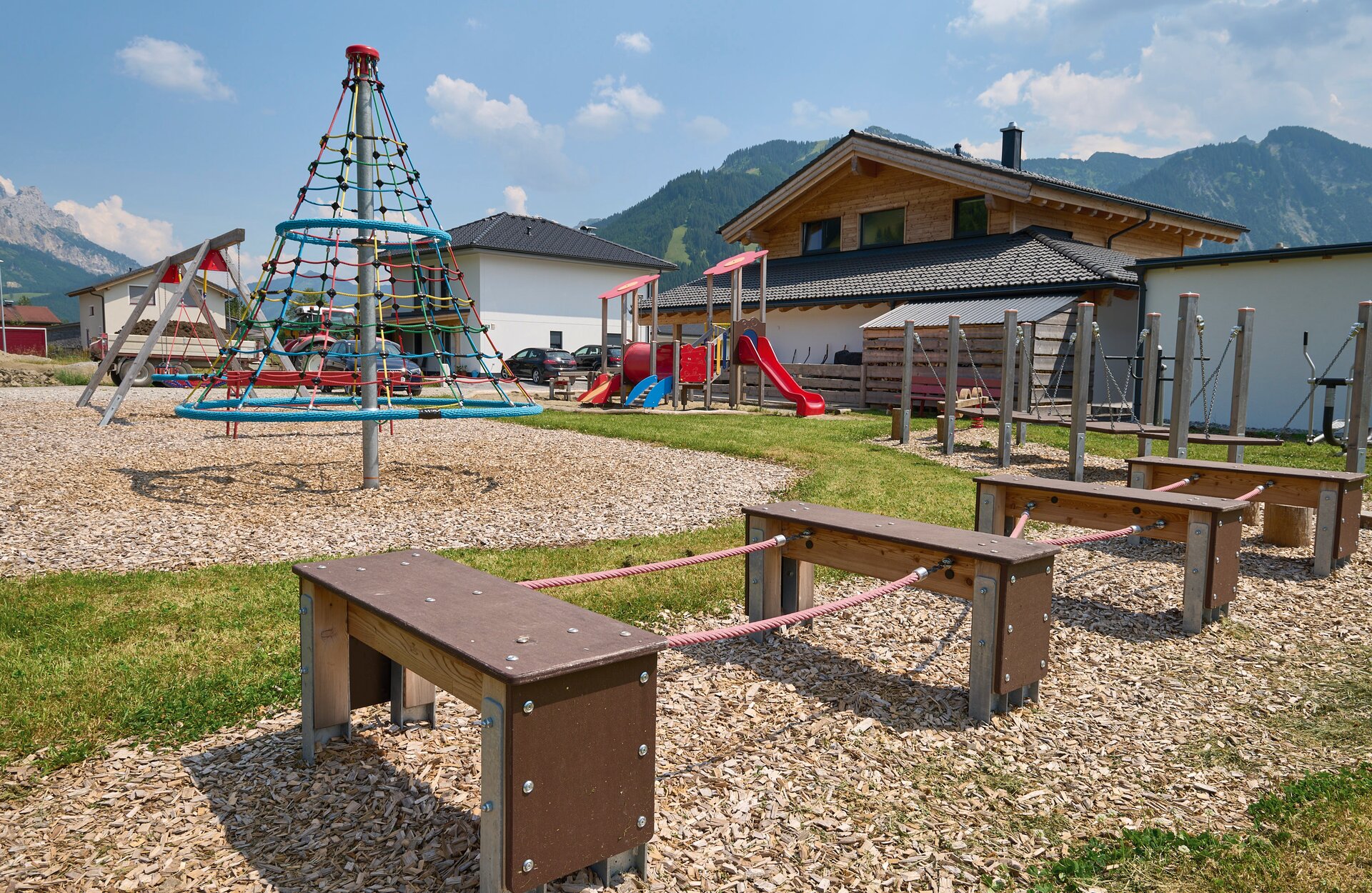 Playground with climbing tower, slide and balance beam against a mountain backdrop