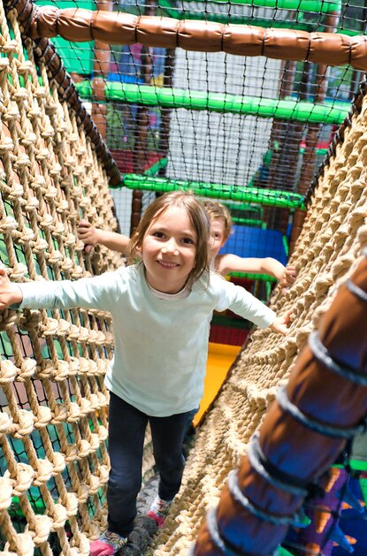 Mädchen balanciert auf Netzbrücke im Indoor-Spielplatz