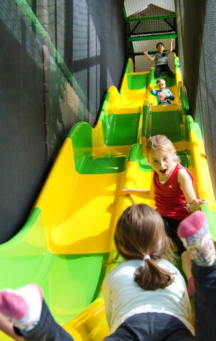 Kinder rutschen auf einer gelb-grünen Rutsche in einem Indoor-Spielplatz