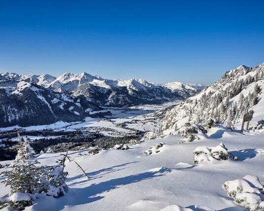 Winterliches Tal mit schneebedeckten Bergen unter blauem Himmel vom Gamskopf aus gesehen