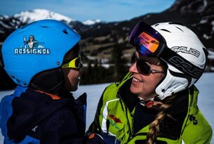 Zwei Skifahrer mit Helmen und Brillen lächeln sich im Schnee an