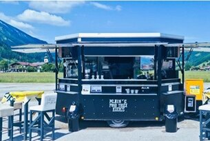 Schwarzer Foodtruck mit Aufschrift vor Bergkulisse