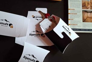 Alpensafe-Verpackungen, Schlüssel, Stift und Infomaterial auf dunklem Untergrund