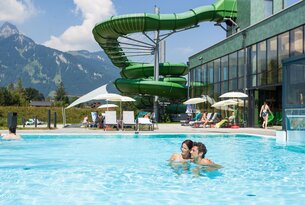 Paar im Pool vor Wasserrutsche und Bergen