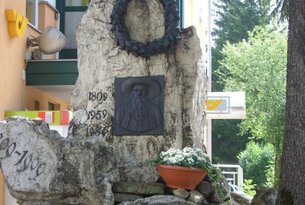 Denkmal mit Adler, Kranz und Relief vor Gebäude