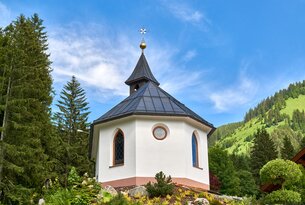 Kleine weiße Kapelle mit schwarzem Dach vor grünem Hügel und blauem Himmel