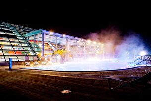 Beleuchtetes Schwimmbad mit Glasgebäude bei Nacht und Nebel