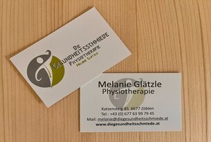 Zwei Visitenkarten der Gesundheitsschmiede Physiotherapie Melanie Glätzle auf Holzuntergrund