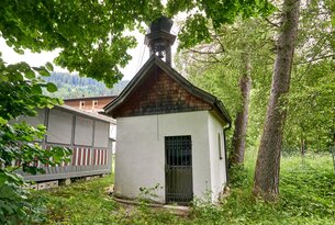 Kleine weiße Kapelle mit braunem Dach und Glockenturm im Grünen