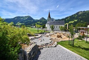 Kirche vor Bergkulisse, Spielplatz im Vordergrund