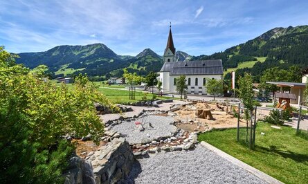 Kirche vor Bergkulisse, Spielplatz im Vordergrund