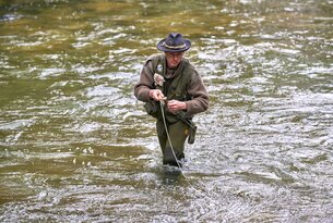Mann mit Hut watet im Fluss und angelt