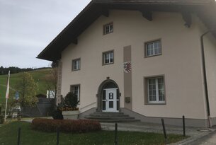 Beiges Gebäude mit dunklem Dach und Wappen über dem Eingang