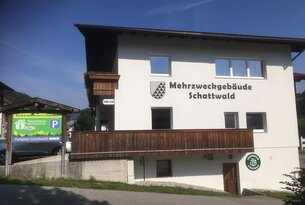 Mehrzweckgebäude Schattwald mit Wappen und Holzverkleidung an Fassade unter blauem Himmel