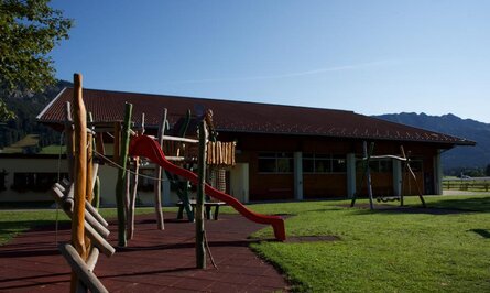 Spielplatz mit Rutsche vor Gebäude mit rotem Dach