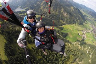 Zwei Personen beim Tandem-Gleitschirmfliegen vor Berglandschaft