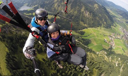 Zwei Personen beim Tandem-Gleitschirmfliegen vor Berglandschaft