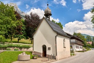 Kleine weiße Kapelle mit Glockenturm vor Bergkulisse