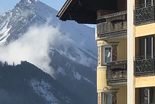 Gelbes Gebäude mit Balkonen vor verschneitem Bergpanorama