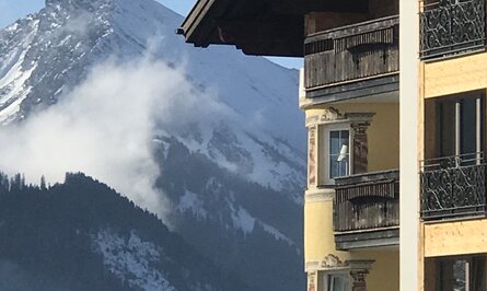 Gelbes Gebäude mit Balkonen vor verschneitem Bergpanorama