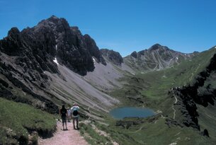 Wanderer auf Bergpfad mit Blick auf See und Berglandschaft