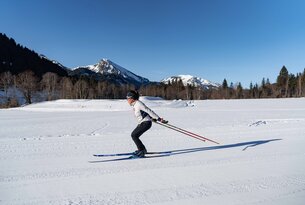 Langläuferin auf schneebedeckter Fläche vor Bergkulisse