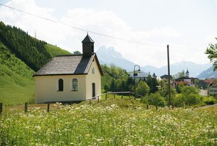 Kleine Kapelle auf Wiese vor Bergkulisse