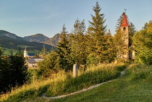 Dorfansicht mit Kirche, Bergen und Wiese im Vordergrund