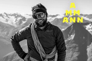 Lächelnder Mann mit Sonnenbrille, Stirnband und Seil vor Bergkulisse