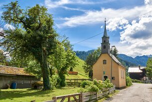 Gelbe Kirche vor grüner Hügellandschaft unter blauem Himmel