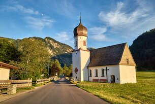 Kirche mit Zwiebelturm vor Bergkulisse an sonnigem Tag