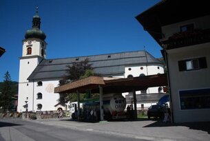 Tankstelle mit Tankwagen vor Kirche unter blauem Himmel
