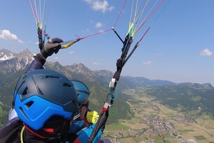 Gleitschirmflug über Berglandschaft mit Blick auf Tal und Ortschaft