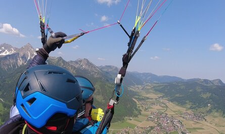 Gleitschirmflug über Berglandschaft mit Blick auf Tal und Ortschaft