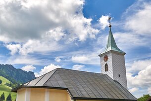 Gelbe Kirche mit Kirchturm unter blauem Himmel mit Wolken vor grünen Hügeln