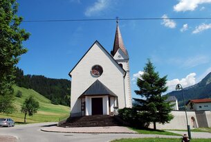 Weiße Kirche mit Kirchturm vor blauem Himmel und grüner Landschaft
