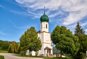 Kirche mit grünem Zwiebelturm vor blauem Himmel und Bäumen