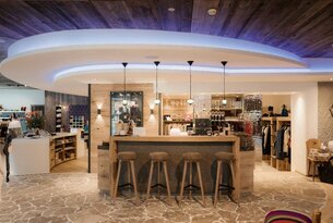 Holzverkleidete Bar mit vier Hockern in einem Raum mit Steinboden und Deckenbeleuchtung