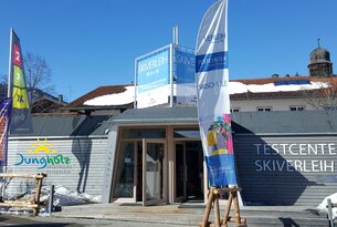 Skiverleih-Gebäude mit Fahne und Schildern vor blauem Himmel