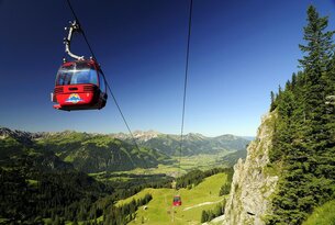 Rote Gondelbahn vor Berglandschaft mit grünen Wiesen und blauem Himmel