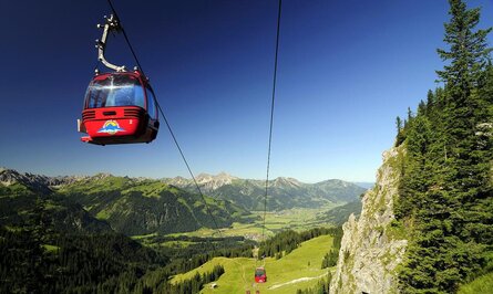 Rote Gondelbahn vor Berglandschaft mit grünen Wiesen und blauem Himmel