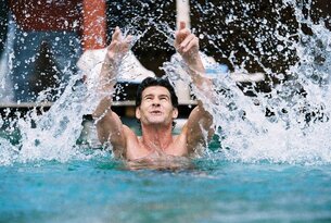 Mann im Wasser wirft Arme hoch, Wasser spritzt