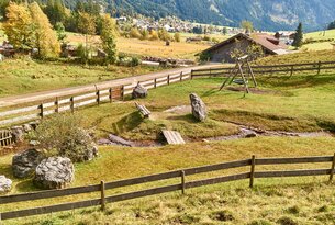 Ländliche Szene mit Holzzaun, Spielplatz, Bachlauf und Bergen im Hintergrund